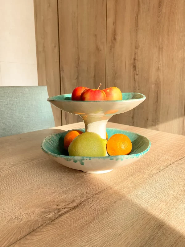 Frutero encima de mesa con manzanas, naranjas y limones con un rayo de luz entrando por la ventana